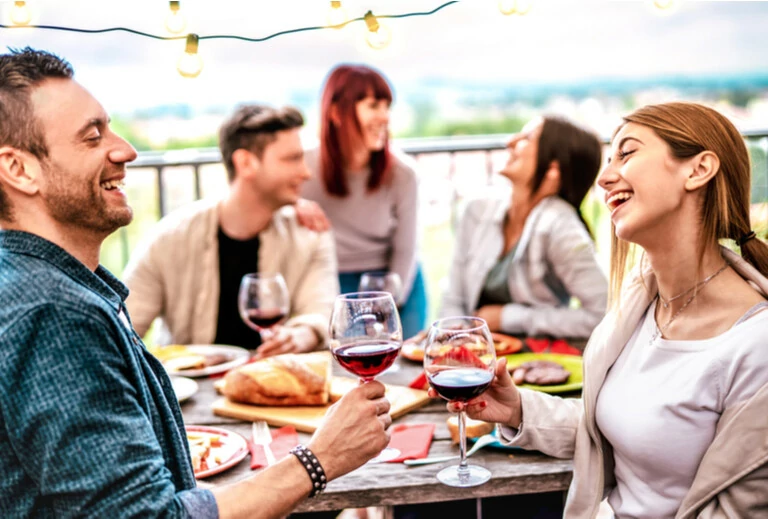 Fröhliche Leute, die auf der Terrasse bei der privaten Dinner-Party Wein trinken können - Junge Freunde, die zusammen Grillspeisen im Restaurant essen - Dinning Lifestyle-Konzept auf warmen Filter - Fokussieren Sie sich auf das richtige Glas