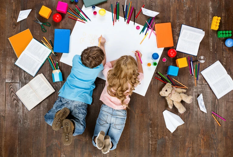 Fröhliche Kinder. Kinder, die umgeben von Büchern und Spielzeug auf dem Boden liegen und auf ein Blatt Papier zeichnen.
