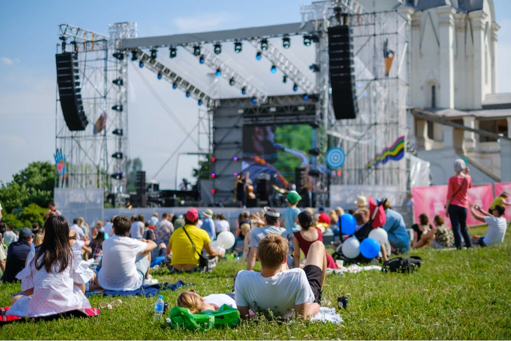 Menschen sitzen gemütlich auf Wiese und schauen sich das Outdoor Konzert an