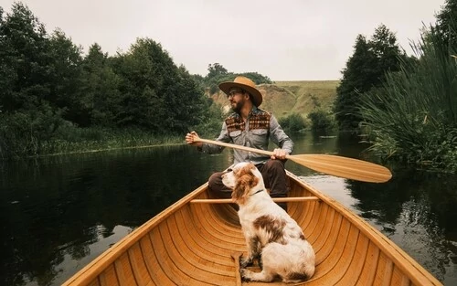 Mann und sein Hund im Kanu aus Holz.