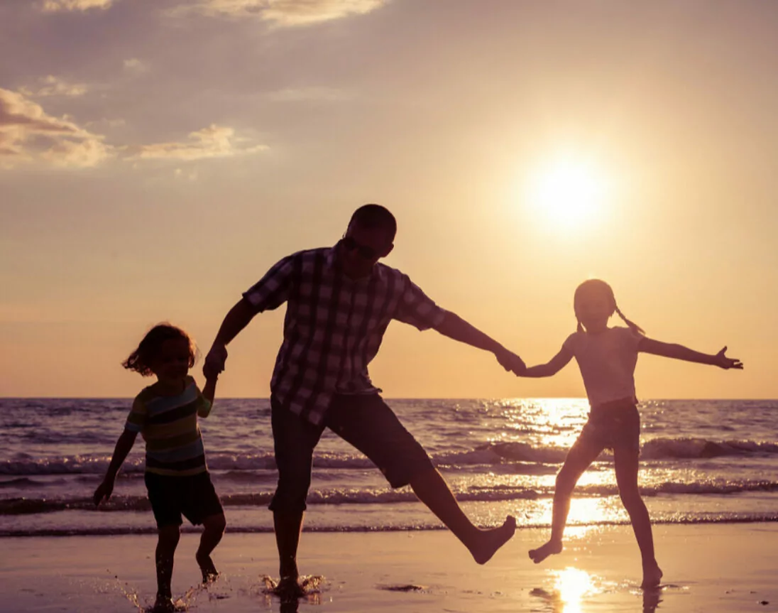 Vater mit Kindern am Strand bei Sonnenuntergang